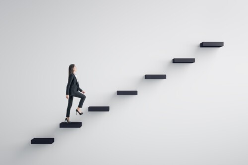 Side view of young businesswoman climbing stairs to success on concrete wall background. Leadership and career development concept