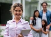 real estate agent holding clipboard in front of sold house