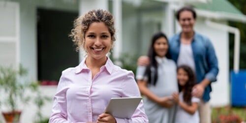 real estate agent holding clipboard in front of sold house