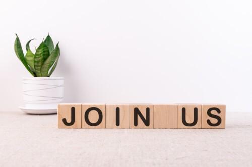 Join us sign on wooden cubes on a light table with flower and light background.