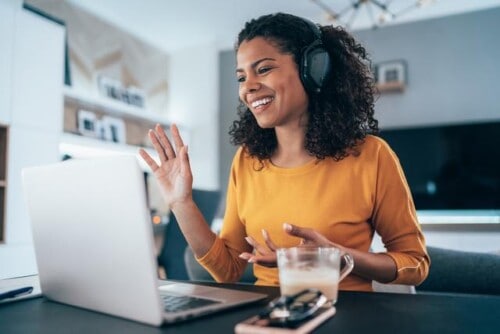 Woman waves to computer screen while making a video