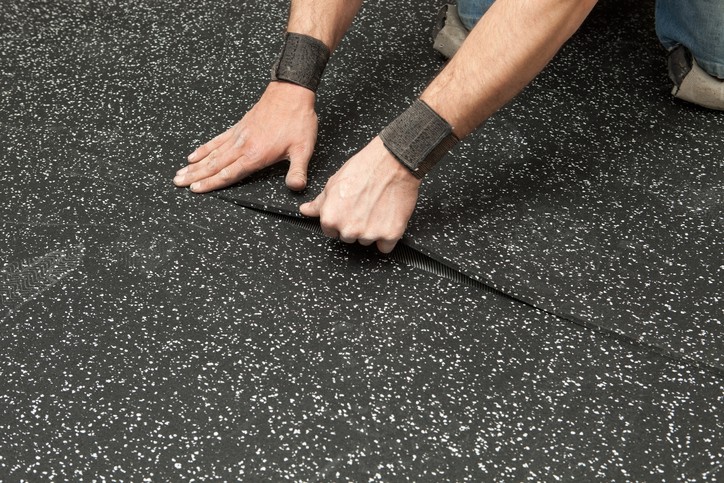 "A worker is installing two sections of a recycled rubber floor. This type of flooring is used in commercial applications which require a padded surface or  electrostatic discharge (ESD) protection. Rubber flooring is popular in fitness centers, entrances, locker rooms, sales floors and ESD sensitive areas. The worker has wrist bands to ease Carpal Tunnel discomfort and prevent tendonitis."