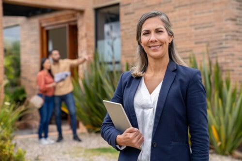 Pleased female real estate agent in front of home showing to couple